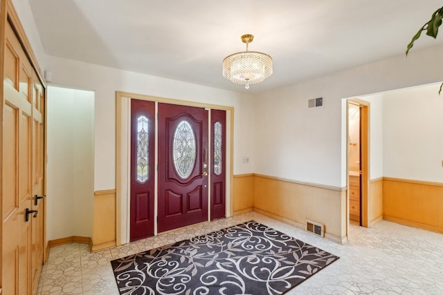 foyer entrance with a chandelier, wooden walls, wainscoting, and visible vents