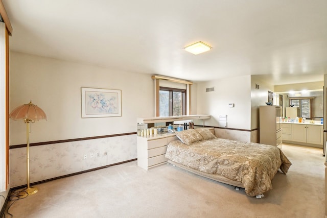 bedroom with baseboards, visible vents, ensuite bathroom, and light carpet