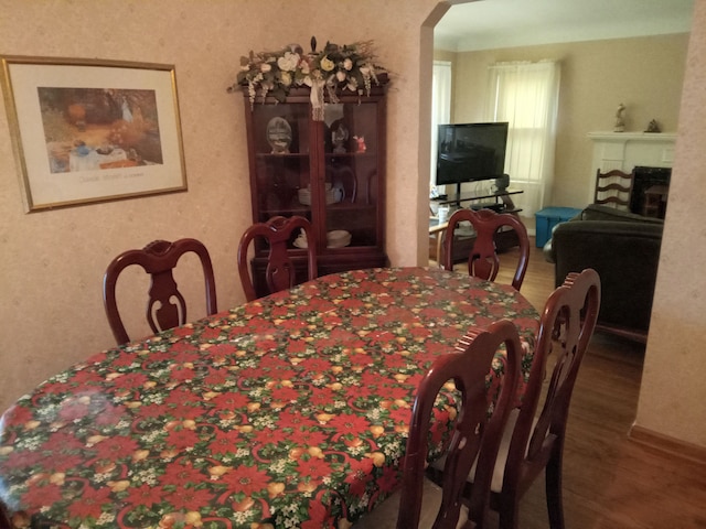 dining area featuring arched walkways, wood finished floors, and a fireplace