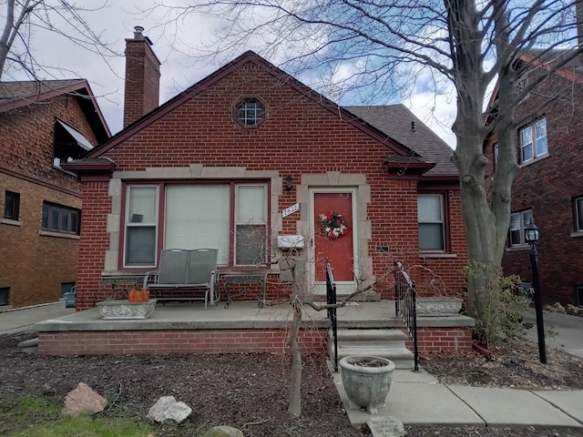 bungalow featuring brick siding, a chimney, and a shingled roof