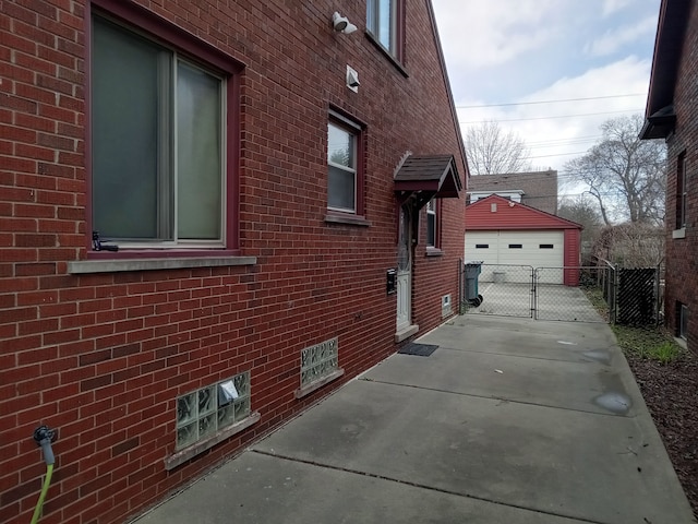 view of property exterior with an outbuilding, a gate, a detached garage, fence, and brick siding