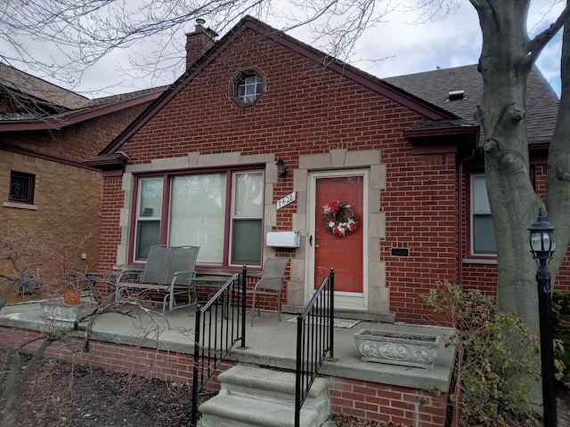 view of front of home with brick siding, roof with shingles, and a chimney