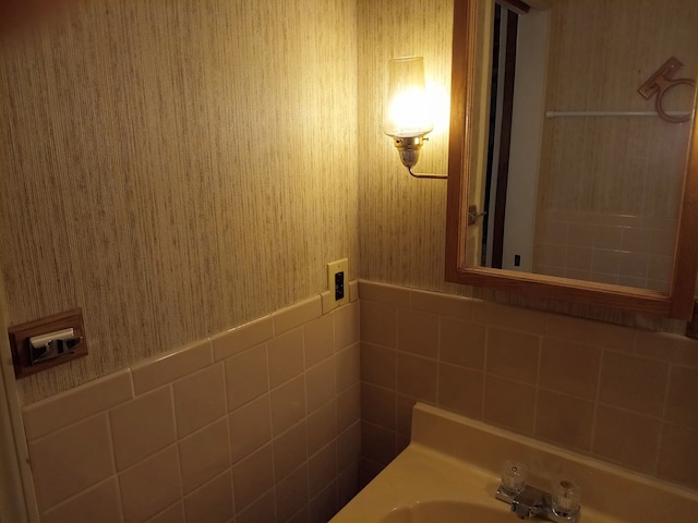 bathroom featuring a wainscoted wall, wallpapered walls, tile walls, and a sink