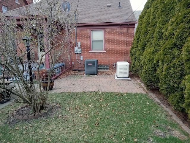 rear view of property featuring brick siding, roof with shingles, central AC unit, a lawn, and a patio