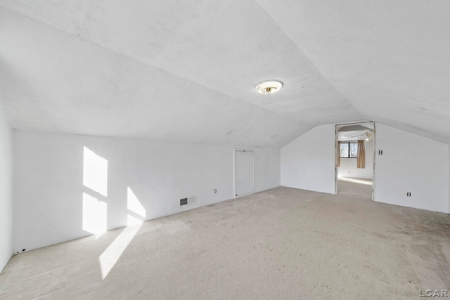 bonus room featuring lofted ceiling, carpet, visible vents, and a textured ceiling