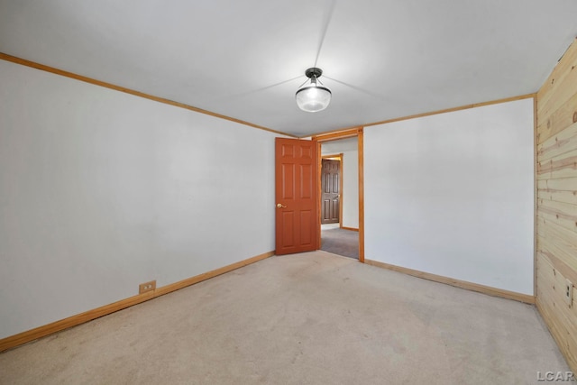 empty room featuring wooden walls, carpet flooring, crown molding, and baseboards