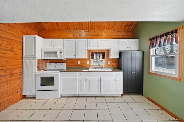 kitchen with a sink, white appliances, wood walls, and light tile patterned floors