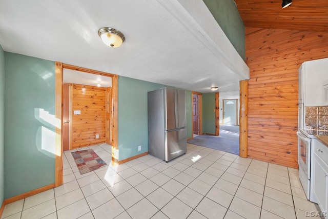 kitchen featuring light tile patterned floors, baseboards, wood walls, and freestanding refrigerator