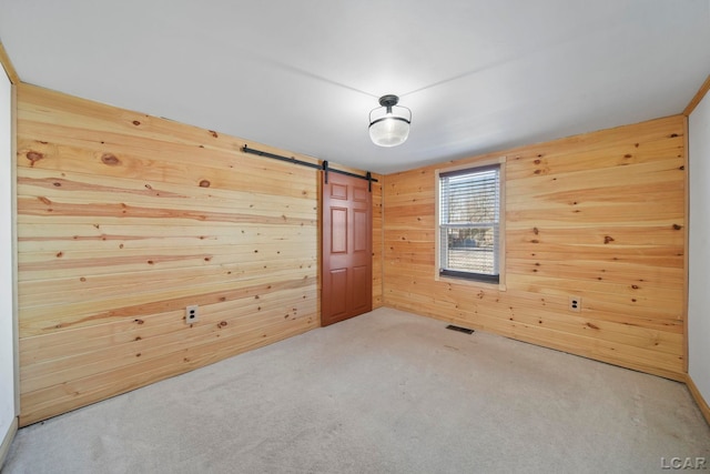 spare room with a barn door, carpet flooring, visible vents, and wood walls