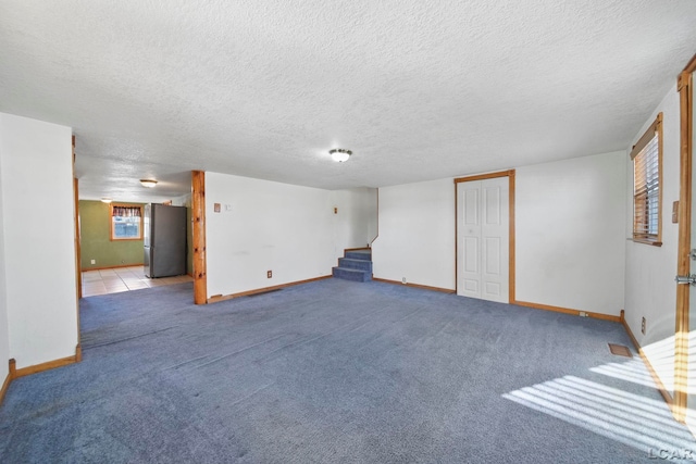 below grade area featuring a textured ceiling, freestanding refrigerator, carpet, baseboards, and stairs