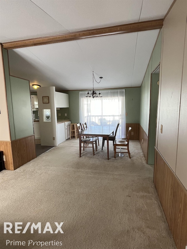 carpeted dining room featuring a notable chandelier, wooden walls, vaulted ceiling with beams, and wainscoting