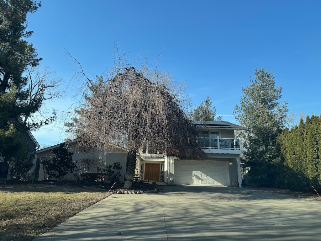 view of property hidden behind natural elements with stucco siding, solar panels, concrete driveway, and an attached garage