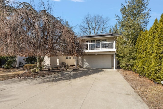 view of front of home featuring roof mounted solar panels, stucco siding, a balcony, a garage, and driveway