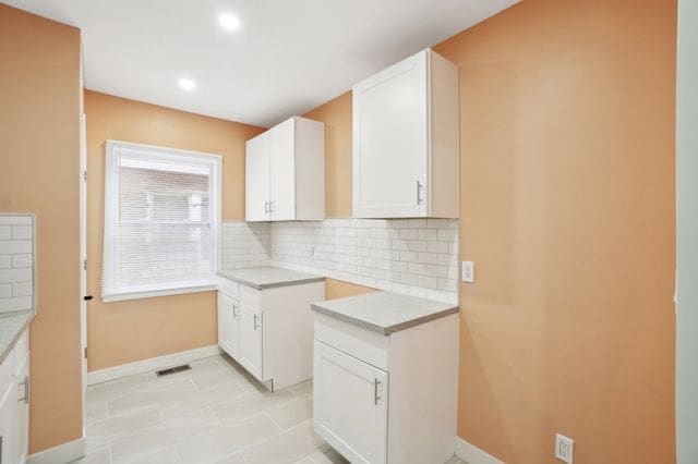 kitchen featuring decorative backsplash, light countertops, baseboards, and white cabinetry