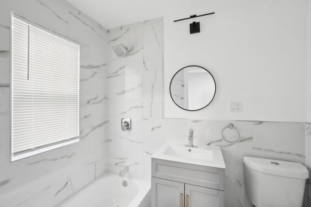 bathroom with vanity, tile walls, toilet, and tub / shower combination