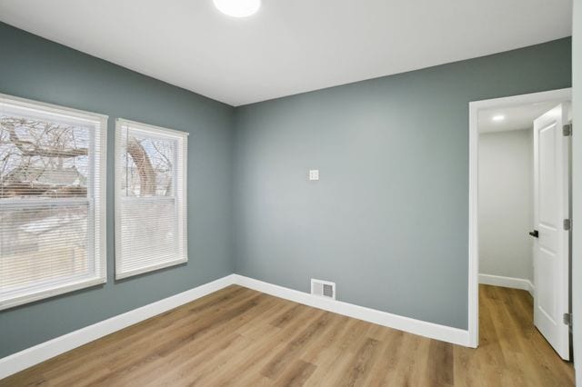 empty room featuring visible vents, light wood-type flooring, and baseboards