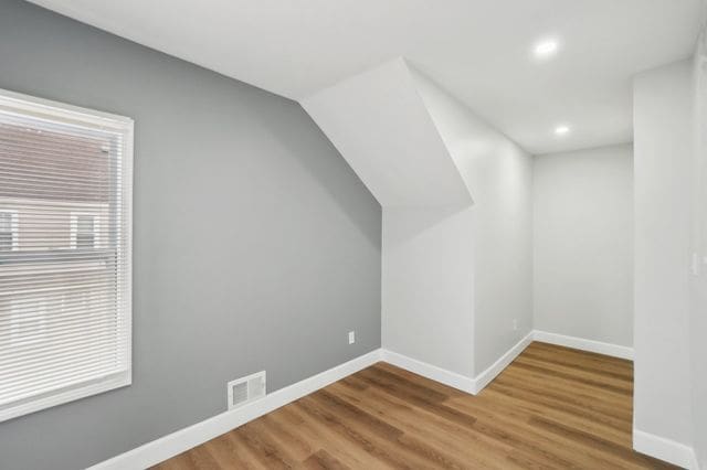 additional living space featuring wood finished floors, visible vents, and baseboards