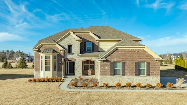 view of front facade with stone siding, brick siding, a front yard, and a shingled roof