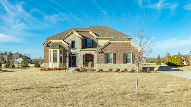 view of front of property featuring a front lawn, brick siding, stone siding, and roof with shingles