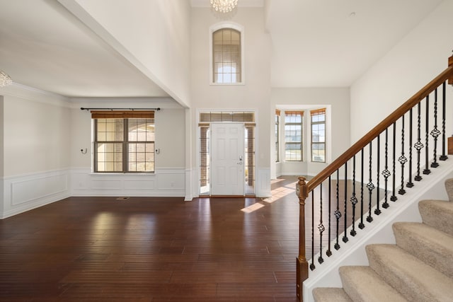 foyer with crown molding, stairs, wainscoting, wood finished floors, and a decorative wall