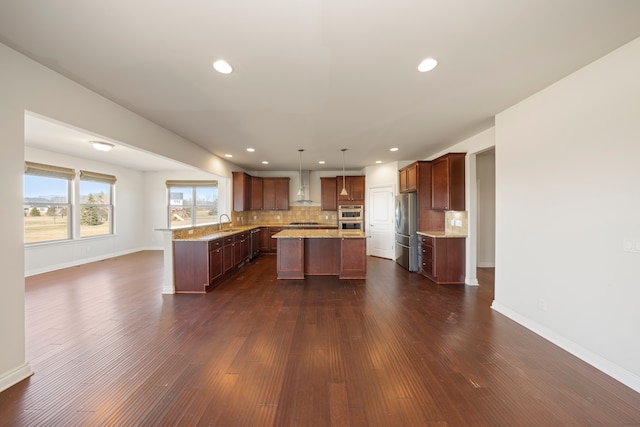 kitchen with a sink, stainless steel appliances, wall chimney range hood, tasteful backsplash, and a center island