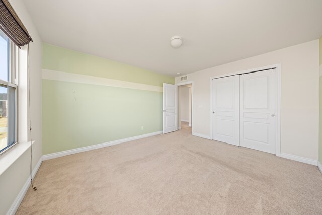 unfurnished bedroom featuring baseboards, visible vents, multiple windows, and light carpet