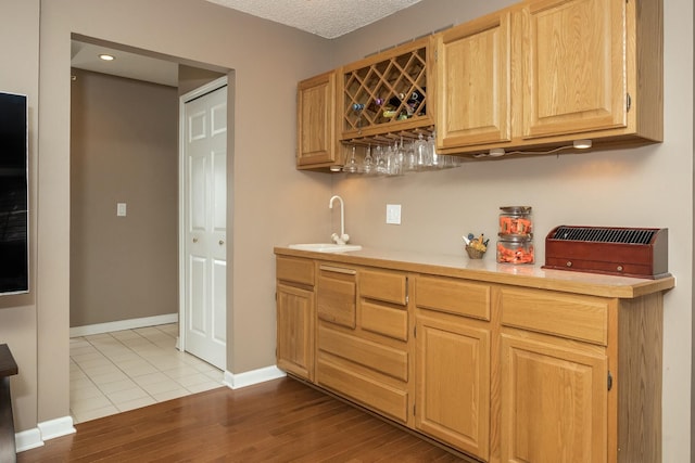bar featuring wet bar, baseboards, wood finished floors, and a sink