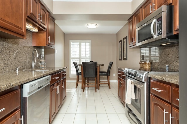 kitchen featuring light stone countertops, a sink, decorative backsplash, light tile patterned floors, and appliances with stainless steel finishes