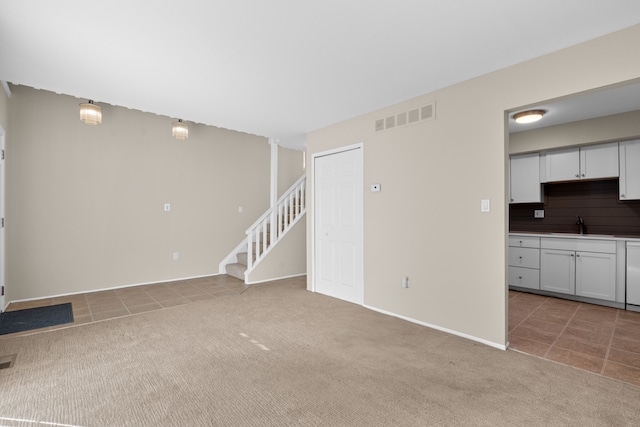 unfurnished living room featuring visible vents, a sink, stairway, light tile patterned floors, and light colored carpet