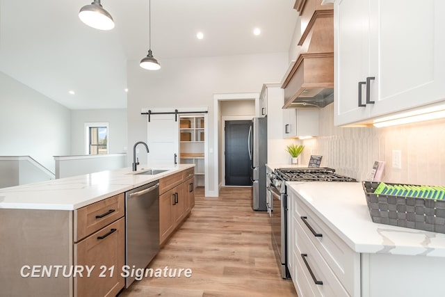 kitchen with premium range hood, a sink, stainless steel appliances, a barn door, and tasteful backsplash