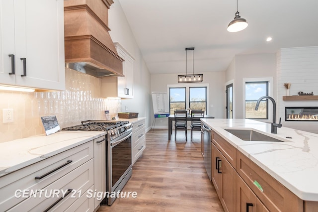 kitchen featuring decorative backsplash, a fireplace, custom exhaust hood, stainless steel appliances, and a sink