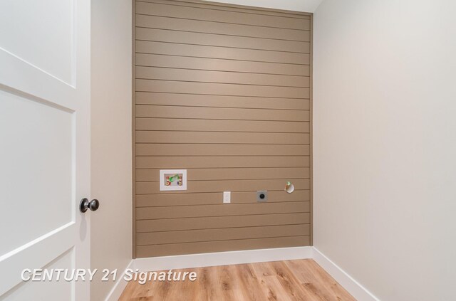 laundry room with light wood-style flooring, wood walls, and laundry area