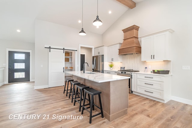 kitchen with a kitchen island with sink, custom range hood, a sink, a barn door, and stainless steel appliances