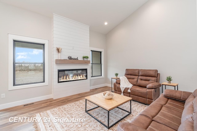 living room with visible vents, a large fireplace, baseboards, lofted ceiling, and wood finished floors