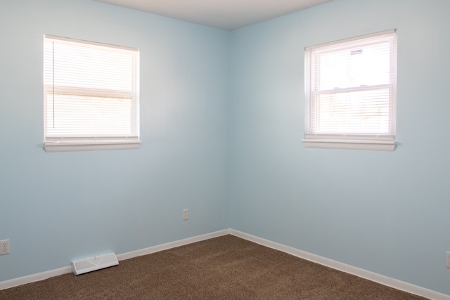 empty room featuring visible vents, dark carpet, and baseboards