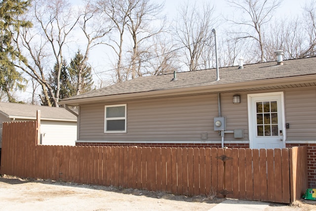 view of home's exterior featuring a shingled roof and fence