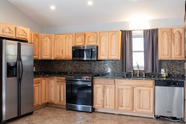 kitchen with lofted ceiling, dark stone countertops, light brown cabinets, and appliances with stainless steel finishes