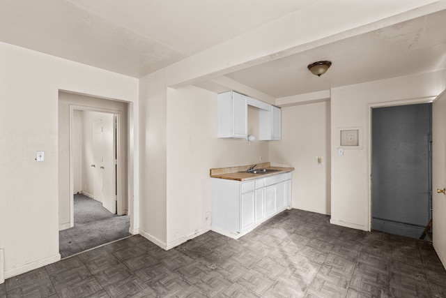 kitchen featuring a sink, white cabinets, dark floors, light countertops, and baseboards