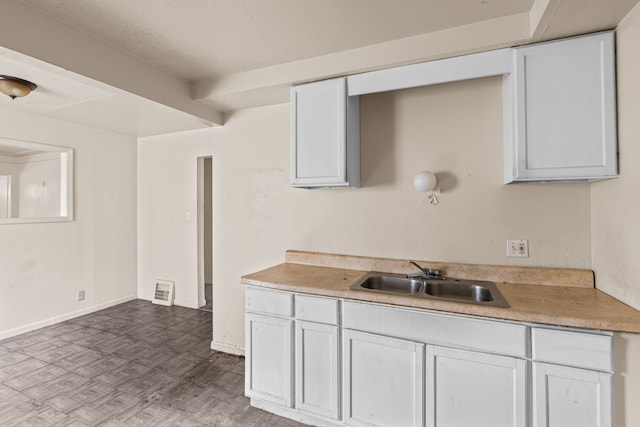 kitchen with white cabinets, light countertops, baseboards, and a sink