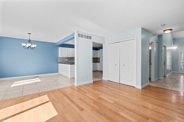 unfurnished living room featuring baseboards, visible vents, a chandelier, and light wood-type flooring