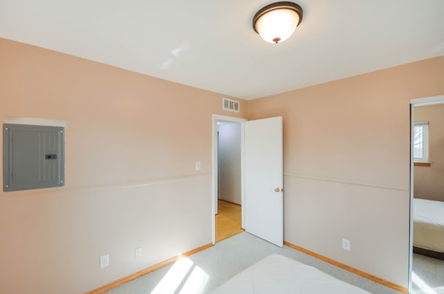 unfurnished bedroom with electric panel, light colored carpet, visible vents, and baseboards