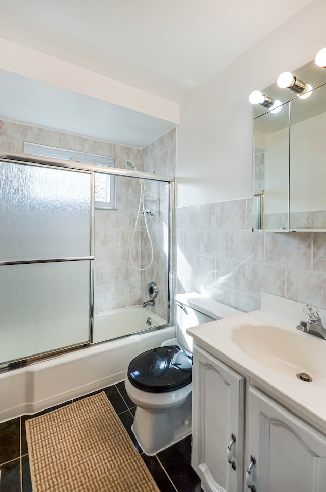 bathroom with tile walls, toilet, tile patterned floors, vanity, and enclosed tub / shower combo