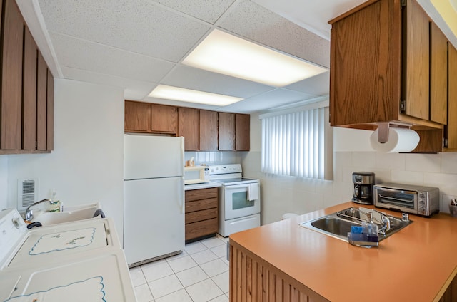 kitchen featuring a toaster, light tile patterned floors, brown cabinetry, white appliances, and washer / clothes dryer