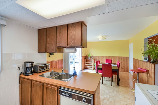 kitchen with white dishwasher, light countertops, wood walls, wainscoting, and brown cabinets