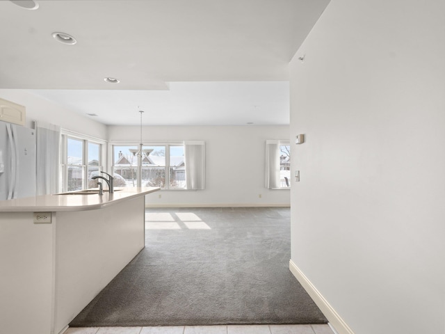 kitchen with baseboards, carpet, light countertops, freestanding refrigerator, and a sink