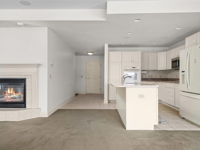 kitchen with light carpet, stainless steel microwave, white refrigerator with ice dispenser, light tile patterned flooring, and a fireplace