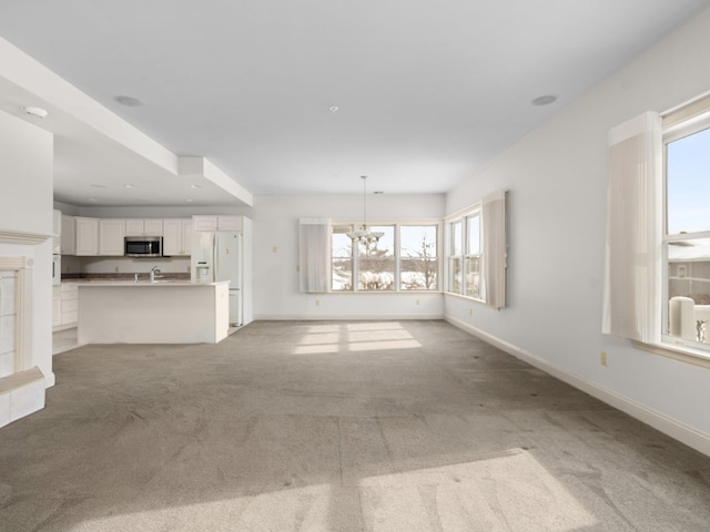 unfurnished living room featuring baseboards, light colored carpet, and a chandelier