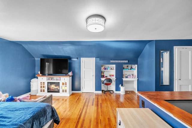 bedroom featuring a glass covered fireplace, wood finished floors, and baseboards