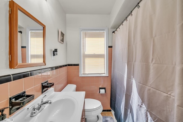 bathroom with tile walls, a wainscoted wall, toilet, a shower with curtain, and vanity