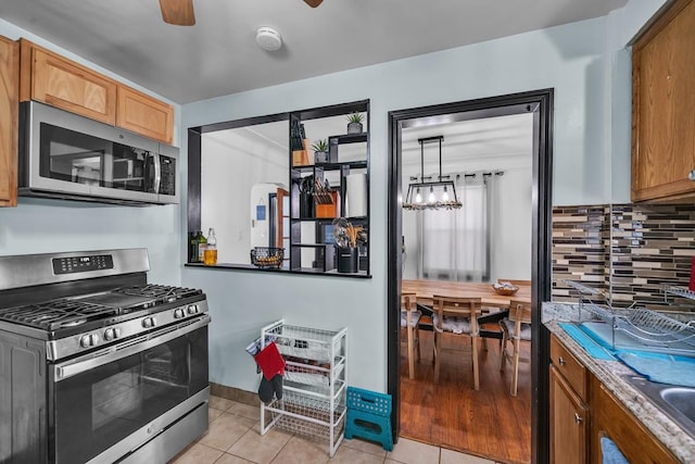 kitchen featuring baseboards, light tile patterned floors, decorative backsplash, appliances with stainless steel finishes, and a ceiling fan